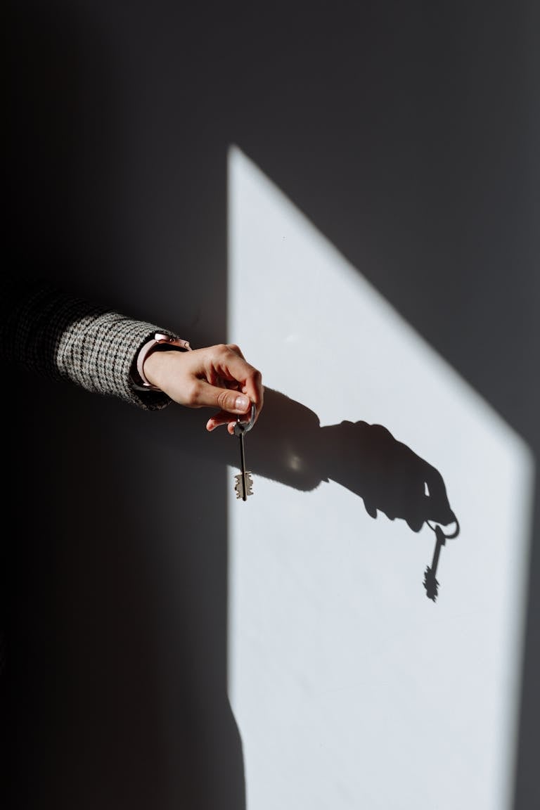 Hand with a key casting a dramatic shadow on a wall, symbolizing property or ownership.