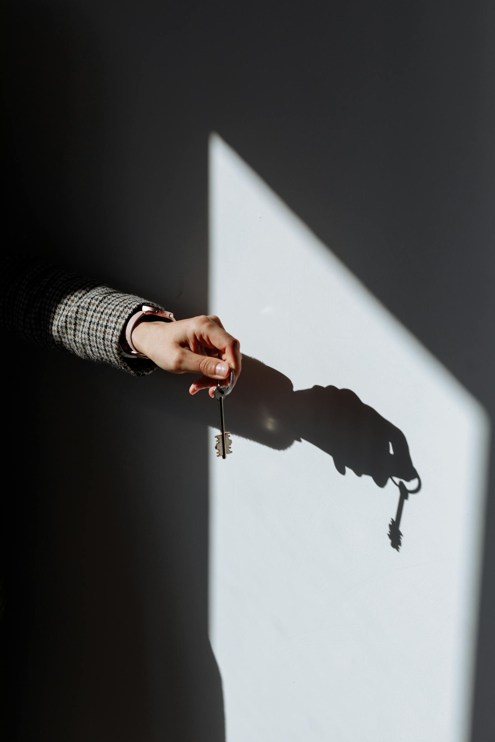 Hand with a key casting a dramatic shadow on a wall, symbolizing property or ownership.